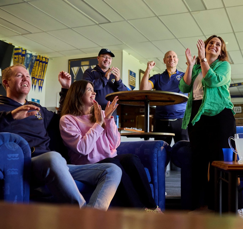 A group of sports fans applauding their team in a living room.