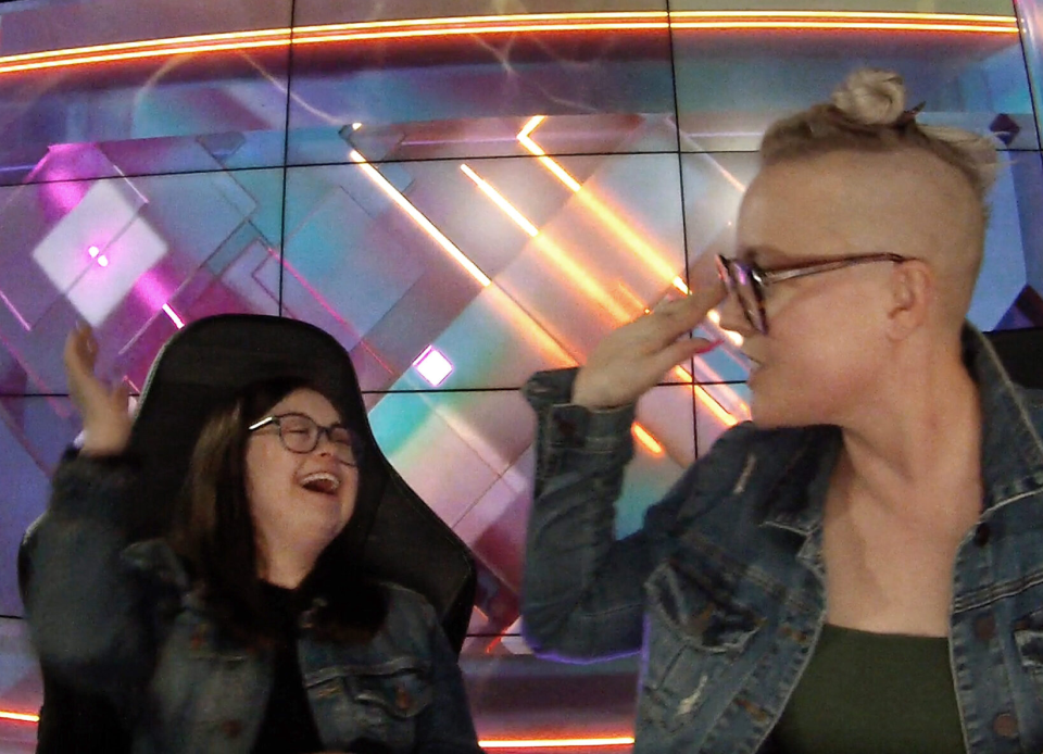 Two people in denim jackets exchanging a high-five in front of a colorful, geometric background.