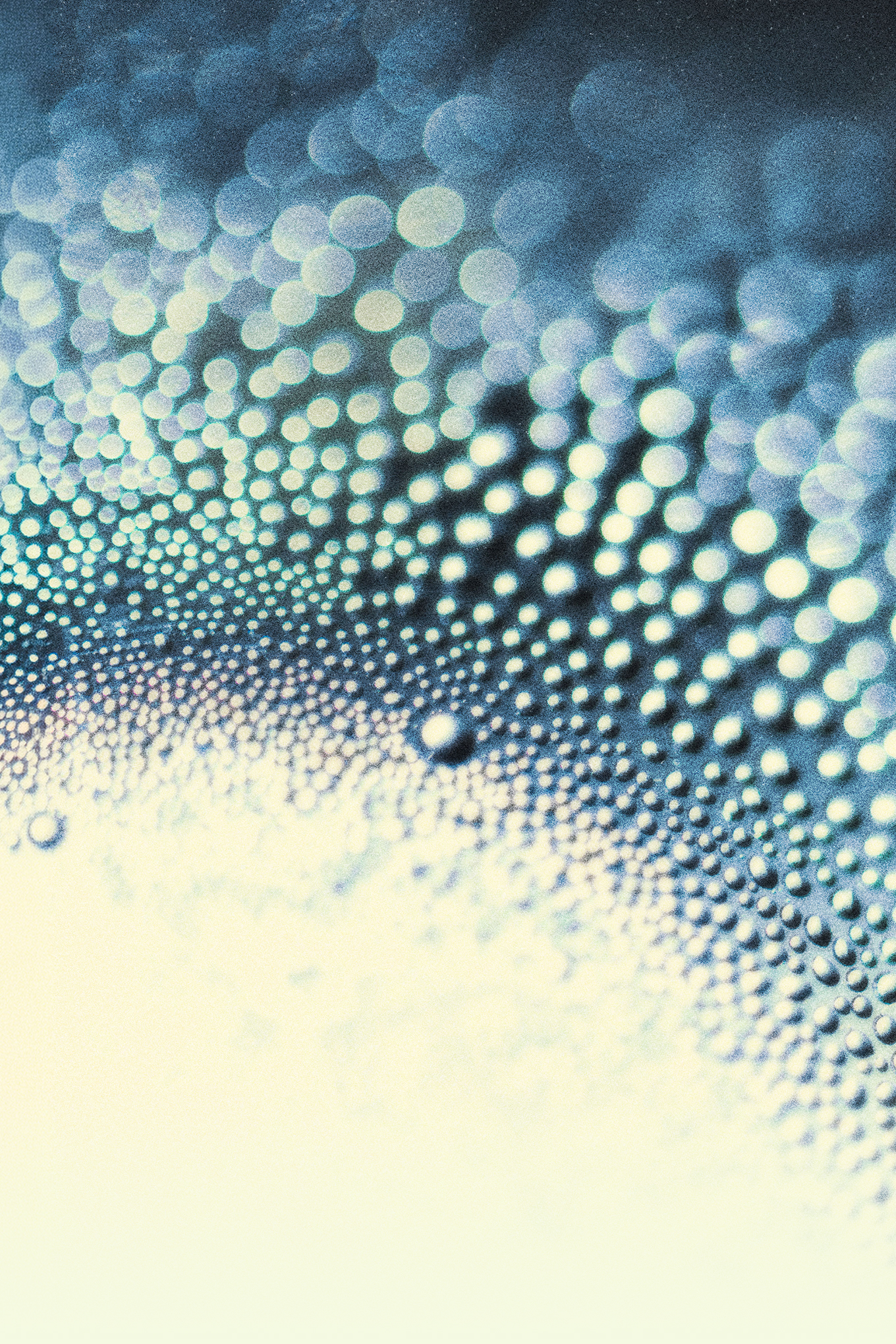 Abstract macro photograph of countless spherical droplets or bubbles arranged in flowing wave-like patterns, rendered in shades of blue, teal, and white with a depth-of-field blur effect.